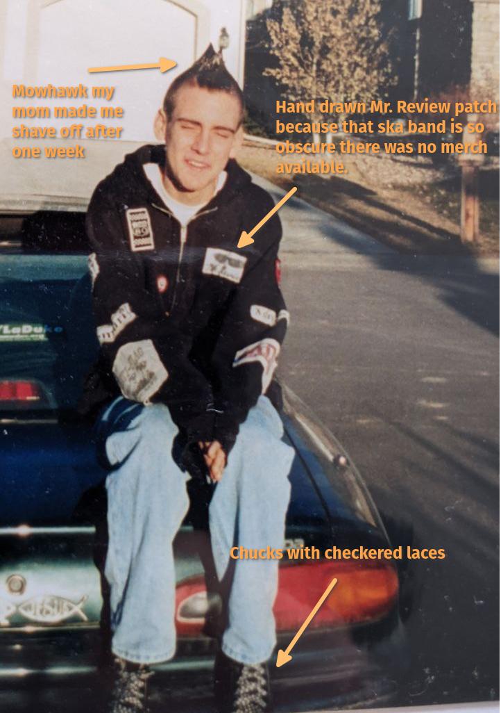 Annotated picture of me as a teenage punk sporting a mowhawk my mom made me shave off after a week, wearing a black hoodie with sewn on patches including a hand drawn one of Mr. Review because they're so obscure you couldn't find their merch anywhere. I'm wearing black Chuck Taylors with checkered shoelaces.