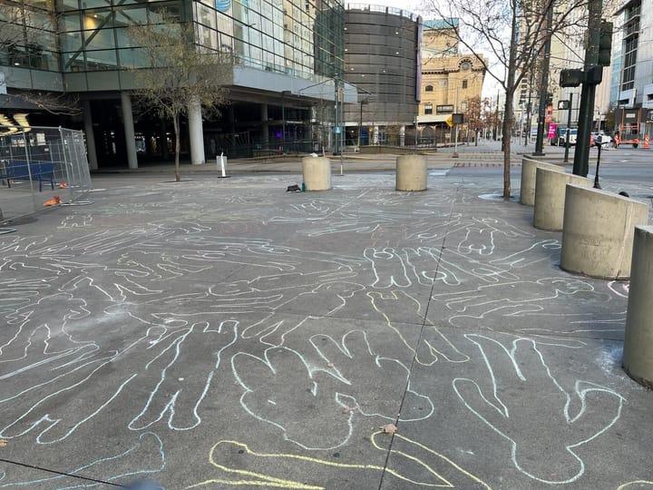 Dozens of chalk outlines of children cover the sidewalk in front of Denver's convention center.